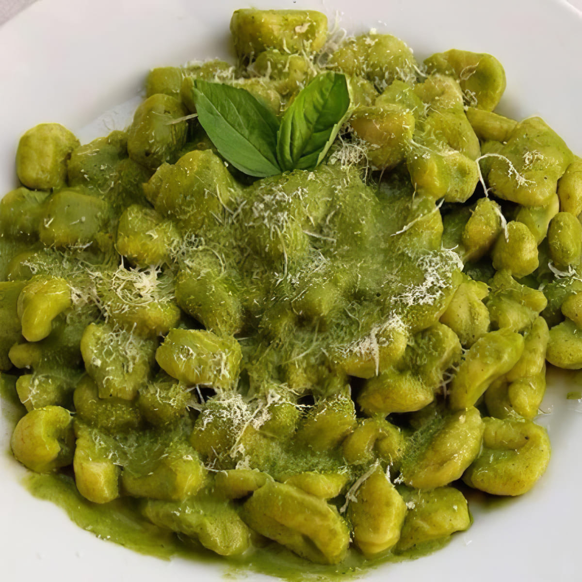 Plato de gnocchi casero verde bañado en salsa pesto y espolvoreado con queso parmesano, listo para llevar en Las delicias del monasterio, Madrid.